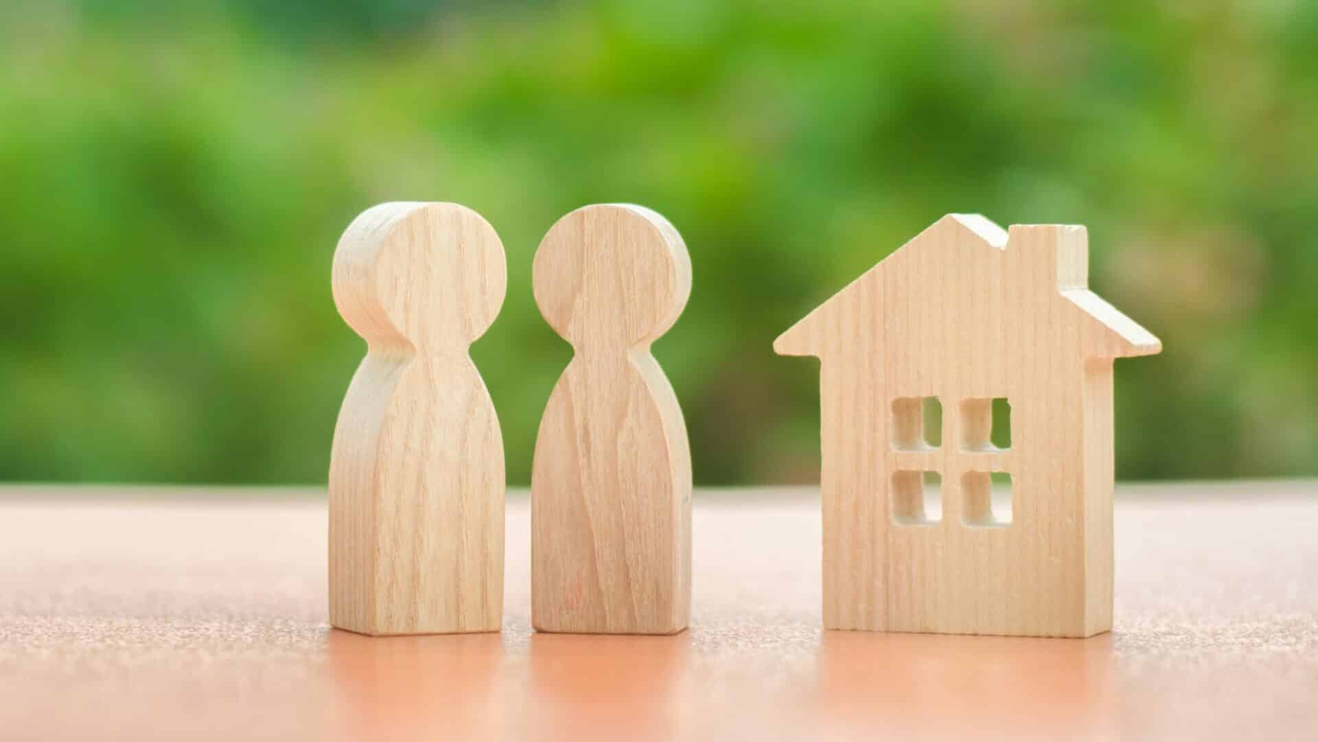 Two wooden figures of people and a house on a nature background. concept of affordable housing, mortgages for buying a home for young families and couples. Buying and selling real estate. Family nest